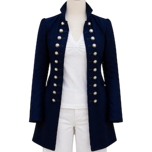 May include: A navy blue military-style jacket with a high collar and double-breasted silver buttons. The long-sleeved jacket is displayed on a mannequin, revealing a white V-neck shirt underneath. The jacket's length extends to the mid-thigh.
