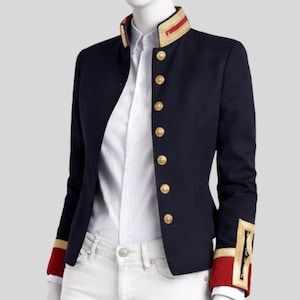 Peut inclure: Veste bleu marine avec boutons et garnitures dorées. La veste présente un col officier avec des accents rouges et dorés, et des détails assortis sur les poignets. Une chemise blanche et un pantalon blanc sont visibles en dessous.