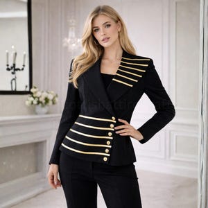 Puede incluir: Una blazer negra con rayas horizontales doradas y botones dorados. La blazer tiene un corte entallado y se combina con pantalones negros. El dise&ntilde;o de la chaqueta incluye rayas doradas en el hombro y en la cintura.