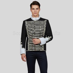 Puede incluir: Chaqueta negra de estilo militar con rayas horizontales y botones plateados. La chaqueta tiene cuello y puños blancos con bordados decorativos. La chaqueta se usa con pantalones azul oscuro.