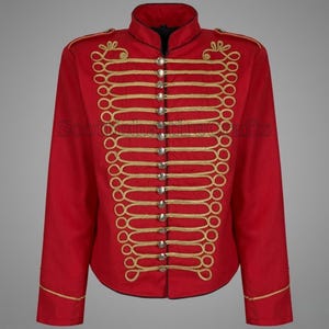 Puede incluir: Chaqueta roja de estilo militar con ribetes y botones dorados. La chaqueta tiene un cuello alto y lazos dorados decorativos en la parte delantera. Las mangas tienen ribetes dorados en los puños. Es una prenda formal.