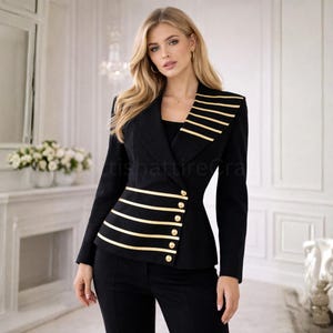 Puede incluir: Una blazer negra con rayas horizontales doradas y botones dorados. La blazer tiene un corte entallado y se combina con pantalones negros. La modelo lleva pendientes de aro dorados.