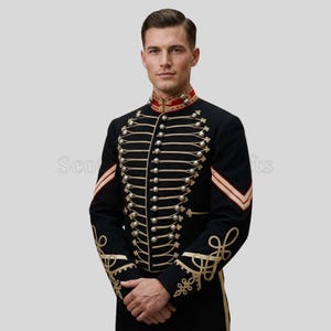 Puede incluir: Chaqueta militar negra con detalles dorados y botones plateados. El cuello alto tiene detalles rojos y dorados, y las mangas presentan bordados dorados. El diseño incluye un frente cruzado y adornos dorados.