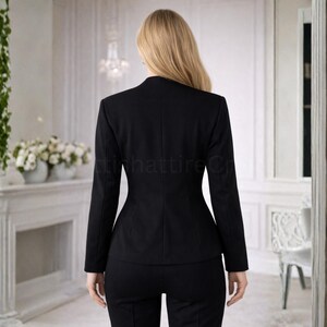 Puede incluir: Un traje negro, compuesto por una blazer entallada y pantalones a juego. La blazer tiene una silueta entallada con solapas y mangas largas. Los pantalones parecen ser de estilo cl&aacute;sico de pierna recta. El traje est&aacute; hecho de una tela oscura y lisa.