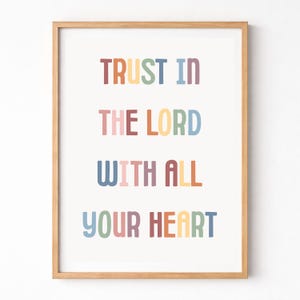 Könnte beinhalten: Ein gerahmter Druck mit dem Text "TRUST IN THE LORD WITH ALL YOUR HEART" in bunten Blockbuchstaben. Der Text ist auf vier Zeilen vor einem weißen Hintergrund angeordnet, und der Rahmen besteht aus hellem Holz.