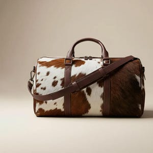 Peut inclure: Sac de voyage en cuir de vache marron et blanc, avec une poignée et une bandoulière en cuir marron. Le sac est rectangulaire et possède une fermeture éclair. Idéal pour les voyages, il a un design classique et rustique.