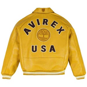 May include: Mustard yellow leather jacket with the text "AVIREX USA" on the back. The jacket has a ribbed collar and cuffs with white and tan stripes. A logo is centered above the text.