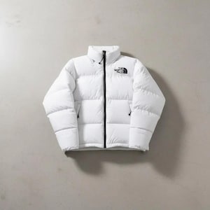 May include: A white puffer jacket with a high collar and black zipper. The jacket has two side pockets and a small black logo on the chest. The North Face logo is visible.