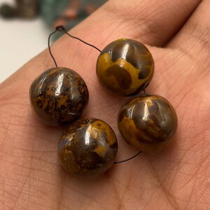 Peut inclure: Quatre perles rondes avec un motif marbré brun et doré, enfilées sur un fil noir. Les perles ont une finition brillante. Les perles sont présentées sur un fond neutre.