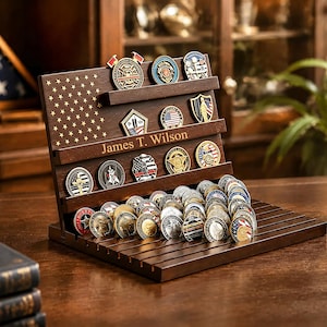 May include: A dark brown wooden display stand for challenge coins, featuring a laser-engraved American flag pattern on the left side and the name James T. Wilson engraved in the centre. The stand has multiple tiered shelves and slots.