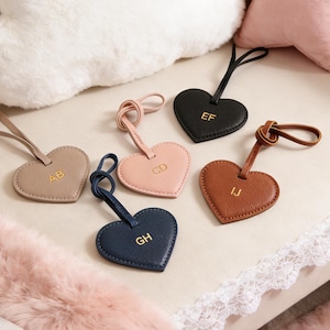 Może przedstawiać: Sześć zawieszek do bagażu w kształcie serca w różnych kolorach: beżowym, różowym, granatowym, czarnym i brązowym. Każda zawieszka ma złotą kombinację inicjałów. Zawieszki mają pętlę do mocowania.