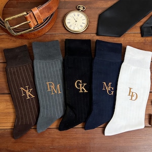 Puede incluir: Un surtido de accesorios masculinos, que incluye cinturón de cuero marrón, reloj de bolsillo, corbata negra y cinco pares de calcetines acanalados de varios colores. Cada calcetín tiene iniciales bordadas. También hay gemelos plateados.