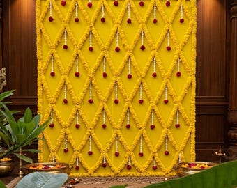 Puede incluir: Un gran telón de fondo rectangular cubierto de flores de caléndula de color amarillo brillante dispuestas en un patrón de rombos. Pequeñas guirnaldas de flores blancas cuelgan verticalmente de cada intersección, con flores rojas oscuras.