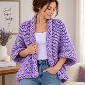 May include: A chunky knit cardigan in a vibrant lavender purple color. This open-front garment features a thick, textured garter stitch pattern, wide three-quarter length sleeves, and a relaxed, loose-fitting silhouette made from thick yarn.