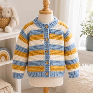 Peut inclure: Un gilet en tricot à manches longues avec des rayures horizontales bleu clair, jaune moutarde et crème. Le vêtement présente un col rond côtelé, des poignets côtelés et une fermeture boutonnée à l'avant avec cinq petits boutons en bois.