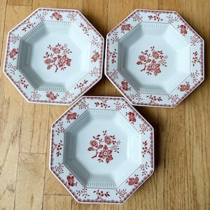 May include: Three white octagonal ceramic bowls featuring a red floral pattern. Each bowl has a central floral motif and a decorative red border along the rim, with vertical ribbed detailing on the interior walls of the basin.