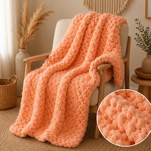 May include: A chunky knit throw blanket in a solid peach color draped over a light-colored armchair. The blanket features a thick, textured yarn construction with large, interlocking loops, visible in both the main view and the circular inset.