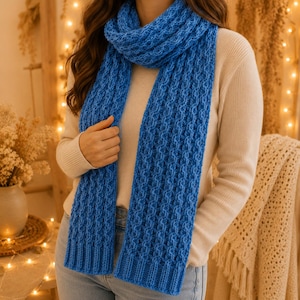 May include: A bright blue knitted scarf featuring a textured cable stitch pattern throughout the length, with ribbed edges at the bottom. The scarf is worn wrapped around the neck, displaying a consistent yarn weight and a vibrant solid colour.