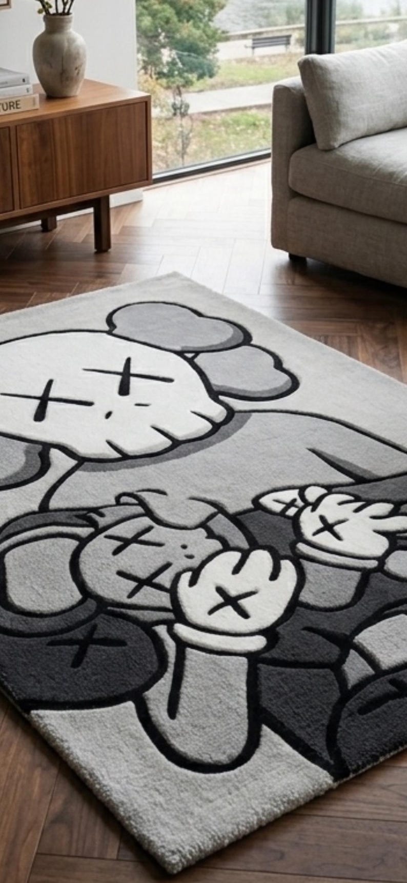 Pu&ograve; includere: Un tappeto rettangolare con una grande grafica di un personaggio dei cartoni animati stilizzato nei toni del grigio, bianco e nero. Il design raffigura due figure con occhi a forma di X e mani guantate, con una texture trapuntata su fondo grigio chiaro.
