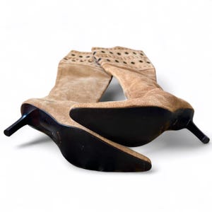 May include: A pair of tan suede boots with pointed toes and stiletto heels. The boots have a perforated design at the top and dark brown soles. The heels are approximately 3 inches tall.