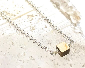 May include: A silver chain necklace with a small gold cube pendant.