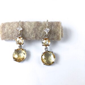 May include: A pair of dangle earrings with two round, faceted, yellow gemstones and a small, clear, faceted gemstone at the top of each earring.