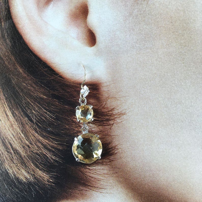 May include: A pair of dangle earrings with two round, faceted, yellow gemstones and a small, clear, faceted gemstone at the top.