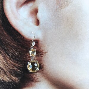 May include: A pair of silver dangle earrings with two round, faceted, yellow gemstones. The earrings have a simple design and are perfect for everyday wear.
