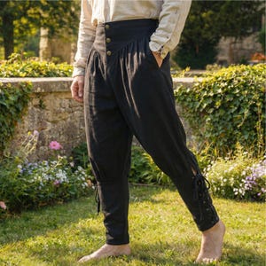 May include: Black high-waisted trousers featuring a wide waistband with three visible buttons, side pockets, and lower leg sections that taper to a fitted cuff with a vertical lace-up closure detail on the outer side of each calf.