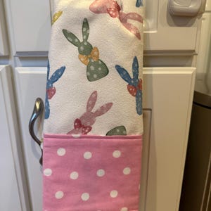 May include: A pink kitchen towel with white polka dots and a white top section with a pattern of colourful bunnies wearing bows.
