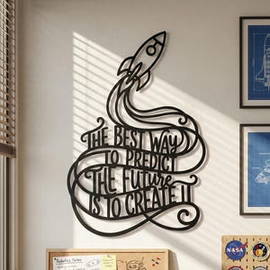 May include: Black metal wall art with a rocket and the quote "THE BEST WAY TO PREDICT THE FUTURE IS TO CREATE IT." The art is above a corkboard with notes and drawings, and a small telescope.