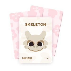 Op de afbeelding: Een kaart met een cartoon skeletgezicht en het woord "SKELETON" in bruine tekst. Het woord "MENACE" staat onder de afbeelding. Twee roze kaarten met een bloemenpatroon staan achter de hoofdkaart.