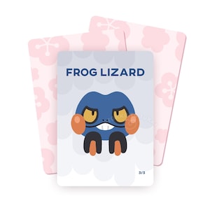 Könnte beinhalten: Ein Satz von drei Karten. Die zentrale Karte zeigt eine blaue Cartoon-froschartige Kreatur mit orangefarbenen Wangen und dem Text "FROG LIZARD". Der Hintergrund ist hellblau mit weißen Wolkenformen. Zwei rosa Karten mit einem floralen Muster befinden sich hinter der Hauptkarte.