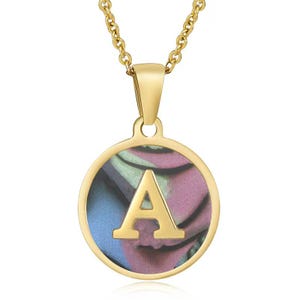 Könnte beinhalten: Goldfarbene Halskette mit einem kreisförmigen Anhänger mit dem Buchstaben "A". Der Anhänger hat einen bunten, marmorierten Hintergrund in Blau-, Lila- und Grüntönen. Die Kette und der Anhängerrahmen sind goldfarben glänzend.