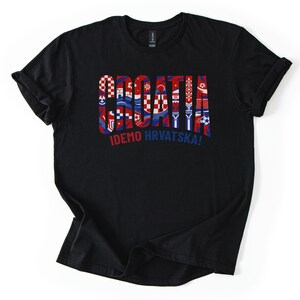 Puede incluir: Camiseta negra con la palabra "CROATIA" en rojo, blanco y azul, con varios dise&ntilde;os inspirados en la bandera croata dentro de las letras. Debajo est&aacute; el texto "IDEMO HRVATSKA!"