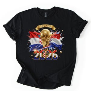 Może przedstawiać: Czarny t-shirt z graficznym wzorem przedstawiającym chorwacką flagę, złoty puchar i napis "CROATIA 2026". Projekt zawiera złote konfetti i transparent.