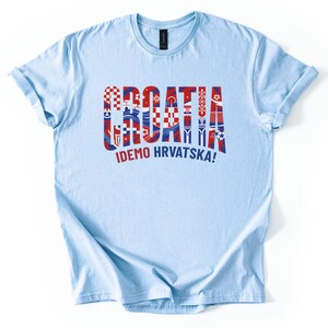 Puede incluir: Una camiseta azul claro con la palabra "CROATIA" en rojo y azul, con dise&ntilde;os inspirados en la bandera croata dentro de las letras. Debajo, la frase "IDEMO HRVATSKA!" en blanco.