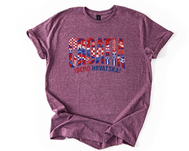 Puede incluir: Una camiseta granate con la palabra "CROATIA" en rojo y azul, dise&ntilde;ada con varios s&iacute;mbolos croatas. Debajo est&aacute; la frase "IDEMO HRVATSKA!" en azul. La camiseta est&aacute; hecha de un material suave.