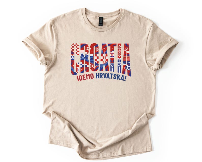 Puede incluir: Camiseta beige con la palabra "CROATIA" en rojo y azul, estilizada con patrones de la bandera croata. Debajo, el texto "IDEMO HRVATSKA!" en rojo. La camiseta es de material suave.