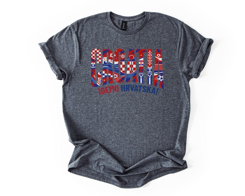Puede incluir: Una camiseta gris jaspeada con la palabra "SOCCER" en rojo, blanco y azul, con dise&ntilde;os inspirados en la bandera croata. Debajo de la palabra "SOCCER" est&aacute; el texto "IDEMO HRVATSKA!" en rojo. La camiseta es de material suave.