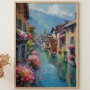 May include: A framed oil painting depicts a European canal scene. Buildings with orange, yellow, and brown facades line the water's edge. Bright pink and red flowers cascade from balconies. The water reflects the sky and buildings.