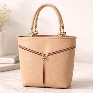 May include: A beige handbag with a textured pattern and a vertical zipper. The bag has a curved top handle and gold-colored hardware. The zipper has a heart-shaped pull. The bag is approximately 10 inches tall.