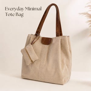 Puede incluir: Bolso tote de lona beige con asas y detalles en cuero marrón. Incluye una pequeña bolsa con cremallera a juego. El texto "Everyday Minimal Tote Bag" está impreso en la esquina superior izquierda. El bolso tiene un diseño minimalista.