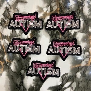 Peut inclure: Cinq écussons brodés noirs et gris avec les mots "Weaponized Autism" en rose et blanc. Chaque écusson a un triangle rose en bas. Les écussons sont disposés sur une surface à motifs de marbre.