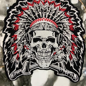 May include: Embroidered patch featuring a skull wearing a Native American headdress. The design incorporates red, white, and black colors, with detailed feather and skull imagery. The patch has a black border and is likely for application on clothing or accessories.