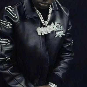 May include: Black leather jacket with white lettering on the sleeves and a patch on the chest. The jacket has a collar and a zipper closure. A silver chain necklace and a watch are also visible.