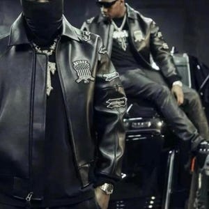 May include: Two people wearing black leather jackets with patches and a black balaclava. The jackets have a bomber style with a collar and are paired with black clothing. One person is wearing a silver watch and a silver chain.