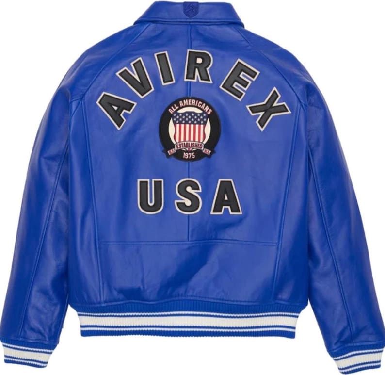 K&ouml;nnte beinhalten: Eine leuchtend blaue Lederjacke mit dem Wort "AVIREX" in wei&szlig;en Buchstaben &uuml;ber den Schultern. Ein kreisf&ouml;rmiger Aufn&auml;her zeigt "ALL AMERICANS" und die US-Flagge. Das Wort "USA" ist darunter prominent platziert.