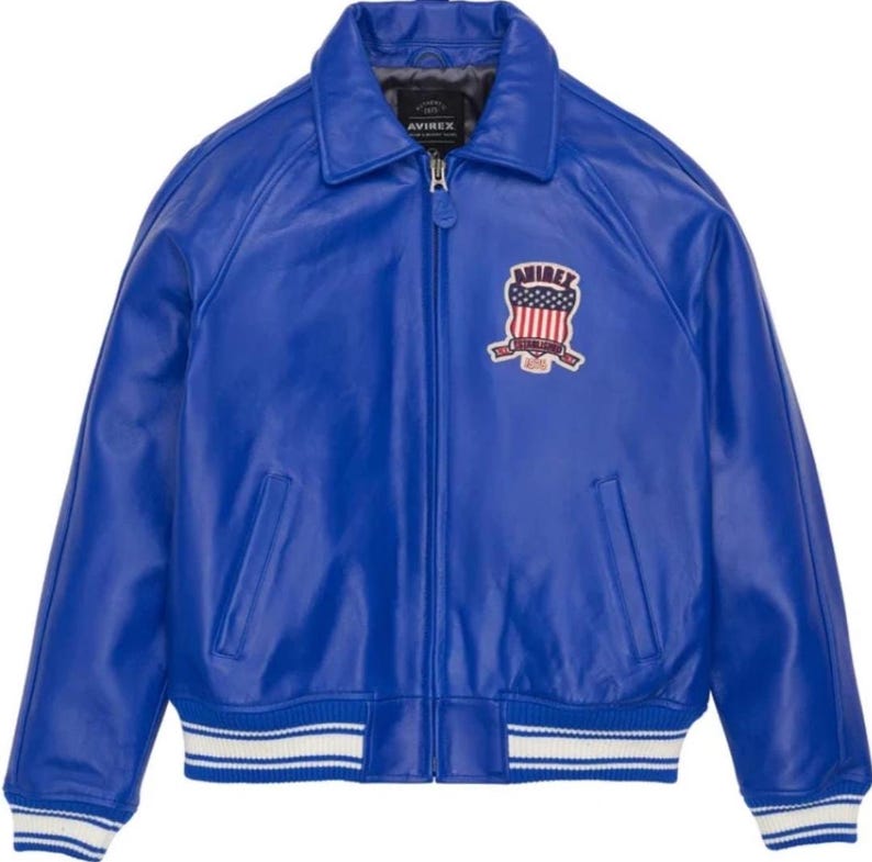K&ouml;nnte beinhalten: Leuchtend blaue Lederjacke mit Rei&szlig;verschluss, Kragen und Brustaufn&auml;her. Die Jacke hat wei&szlig;-blaue gestreifte B&uuml;ndchen und Saum. Der Aufn&auml;her zeigt ein patriotisches Design mit dem Text "AVIREX".