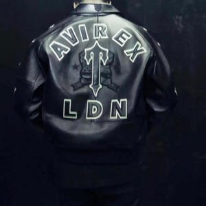 May include: Black leather jacket with white lettering spelling out "AVIREX" and "LDN". A central emblem features a stylized "T" design. The jacket has a classic bomber style.